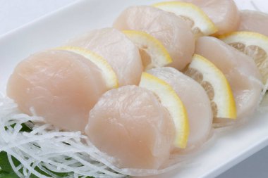 Beyaz tabakta limon dilimleriyle süslenmiş taze hazırlanmış deniz tarakları. 