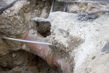 Çamur ve inşaat malzemeleriyle çevrili korunmasız bir yeraltı borusu