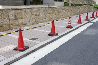 Turuncu trafik konileri taş duvarın yanında boş kaldırımda diziliyor