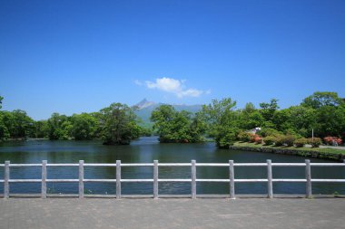 Sakin göl manzarası, yeşil park ve ufuktaki dağlar.