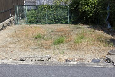 Yeşil çitlerle ve ağaçlarla çevrili kuru boş arazi.