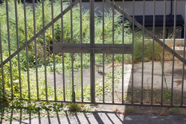 Güneşli metal kapı beton zeminde çizgili gölgeler bırakıyor