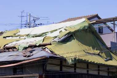 Hasarlı çatı, açık gökyüzünün altında yırtık yeşili gösteriyor.