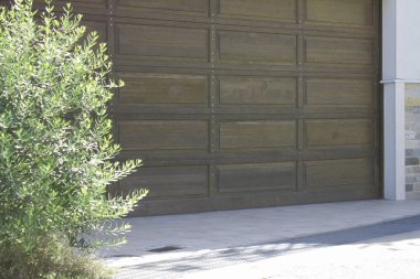 Yeşil çalıların yanında kapalı ahşap bir garaj kapısı.