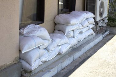 Klima ünitesinin yanındaki duvara beyaz kum torbaları yığılıyor.