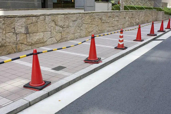 Turuncu trafik konileri taş duvarın yanında boş kaldırımda diziliyor