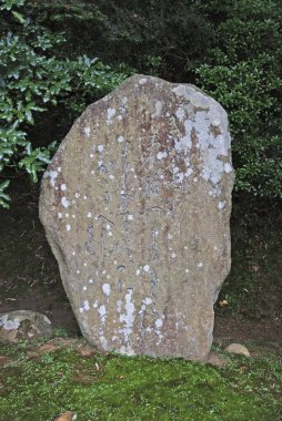 Yeşil yapraklı çalıların arasında duran eskimiş taş bir anıt.