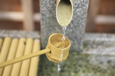 Bambu kepçesi geleneksel taş havzasında akan suyu yakalıyor.