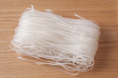 Tahta yüzeyde düzgünce istiflenmiş ince pirinç erişteleri.