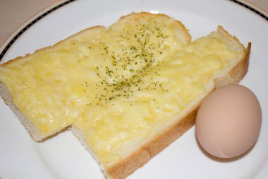 Kaynamış yumurtanın yanında erimiş peynirle kaplı tereyağlı tost dilimleri.