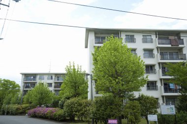 Yeşil ağaçlar ve renkli çiçeklerle çevrili modern binalar.