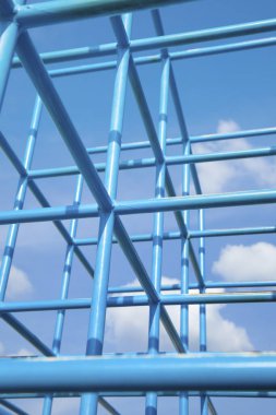 Gökyüzüne karşı geometrik yapı oluşturan mavi metal çubuklar