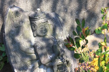 Yıpranmış taş heykel çiçek açan bahçenin yanında gölgeler bırakıyor.