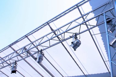 Metal sahne kirişleri parlak gökyüzü altında asılı duran spot ışıklarını destekliyor