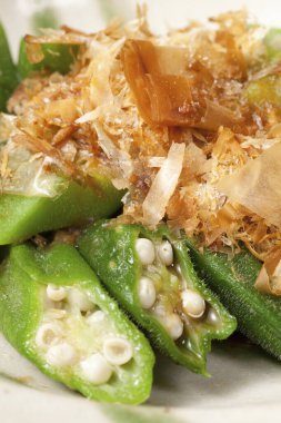 Dilimlenmiş bamya üzerine seramik tabakta bonito taneleri yakın çekim görüntüsü.