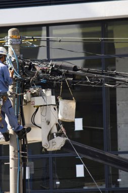 Dışarıdaki beton direğin tepesinde elektrik kablolarını tamir eden bir elektrik işçisi.
