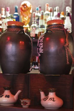 Barda içki şişelerinin yanında duran büyük seramik kavanozlar.