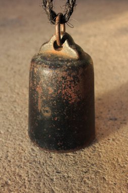 Dışarıda siyah kablodan sarkan paslı metal çan.