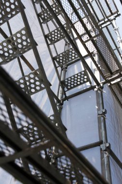 Şehir caddesinde yüksek açılı, dikey bir manzara. Çerçevelenmiş ve binanın dış tarafındaki yoğun yapı iskelesi ve koruyucu ağ tarafından kısmen gizlenmiş..