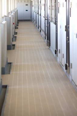 Kapalı beyaz kapılar ve parlak ışıklarla dolu uzun ve boş bir koridor.