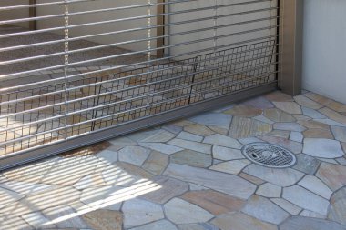 Metal kapı taş verandaya gölge düşürüyor.