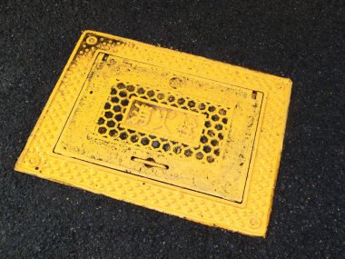 Siyah asfalt yüzeyinde sarı rögar kapağı var.