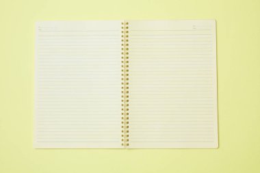 Boş bir defterin üst görünümü, sade sarı bir arkaplanda izole edilmiş..