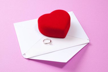 Alyans, kırmızı kalp ve pembe arka planda zarf.        