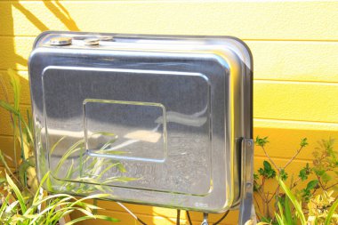 Sarı duvarın yanında güneş ışığını yansıtan parlak metal malzeme kutusu