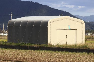Kırsal alanda duran büyük beyaz bir depo.