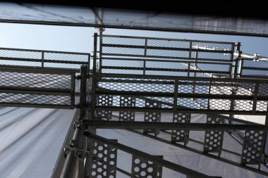 Şehir caddesinde yüksek açılı, dikey bir manzara. Çerçevelenmiş ve binanın dış tarafındaki yoğun yapı iskelesi ve koruyucu ağ tarafından kısmen gizlenmiş..