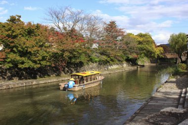 Sarı çatılı bir tur teknesi renkli sonbahar ağaçlarıyla çevrili bir kanalda yol alır..
