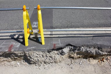 Sarı uyarı barikatı yakınlarında asfalt yol yüzeyinde hasar var.