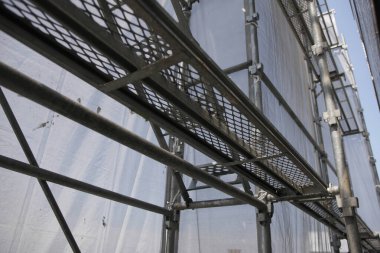 Şehir sokağı, binanın dış tarafındaki yoğun yapı iskelesi ve koruyucu ağ ile çerçevelenmiş ve kısmen gizlenmiş..