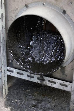 Kalın siyah atık endüstriyel metal boruyu yer yüzeyine döküyor.