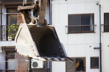 Büyük kazıcı kovası dış binanın yanında asılı duruyor.