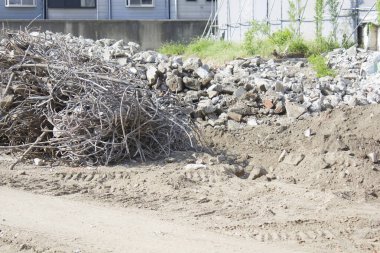Kuru dallar ve inşaat enkazı toprak zeminin yanında yatıyor.
