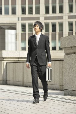 Takım elbiseli ve kravatlı genç bir işadamı sokakta yürüyor. 