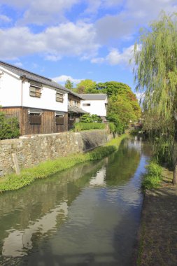 Mavi gökyüzünün altında geleneksel beyaz evlerin yanında akan huzurlu bir kanal.