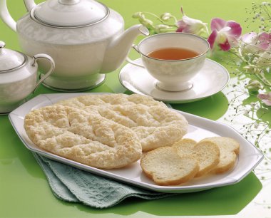 Bir fincan çay, tatlı ekmek, masada bisküvi.