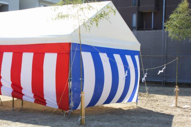 Çizgili kırmızı mavi beyaz festival çadırı güneşli bir günde dışarıda duruyor.