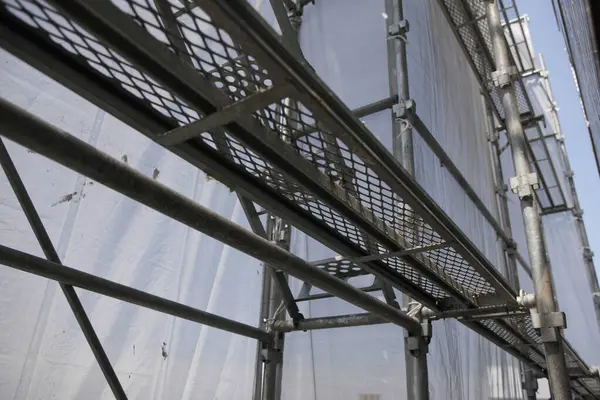 Şehir sokağı, binanın dış tarafındaki yoğun yapı iskelesi ve koruyucu ağ ile çerçevelenmiş ve kısmen gizlenmiş..