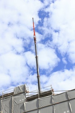 Bulutlu gökyüzüne karşı binanın üzerine uzanan uzun vinç