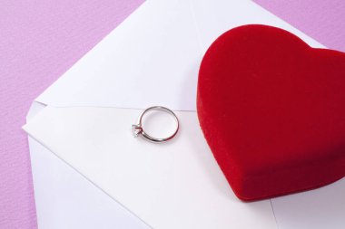 Alyans, kırmızı kalp ve pembe arka planda zarf.        