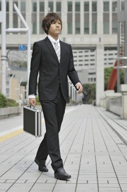 Evrak çantalı Asyalı işadamı sokakta yürüyor. 