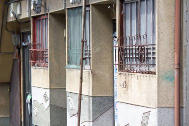 Yıpranmış apartmanın dış tarafı parmaklıklı pencere ve boruları gösteriyor.