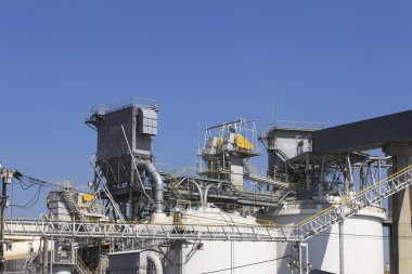 Açık mavi gökyüzü altında metal yapılara sahip endüstriyel bir tesis.