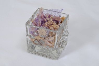 Renkli kurutulmuş çiçek ve taşlarla dolu küçük cam bir kap.