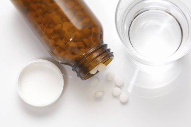 Şişedeki haplar ve beyaz arka planda bir bardak su.