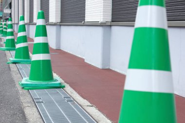 Dış binanın yanında kaldırımda yeşil trafik konileri var.